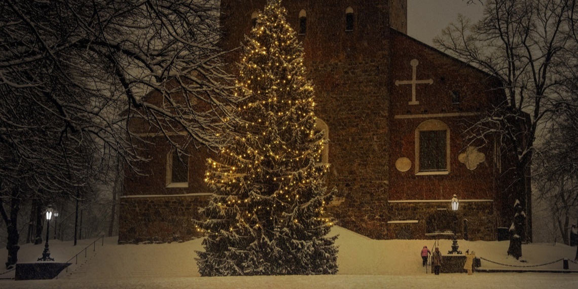 Et juletre med lys i snøvær foran en kirke